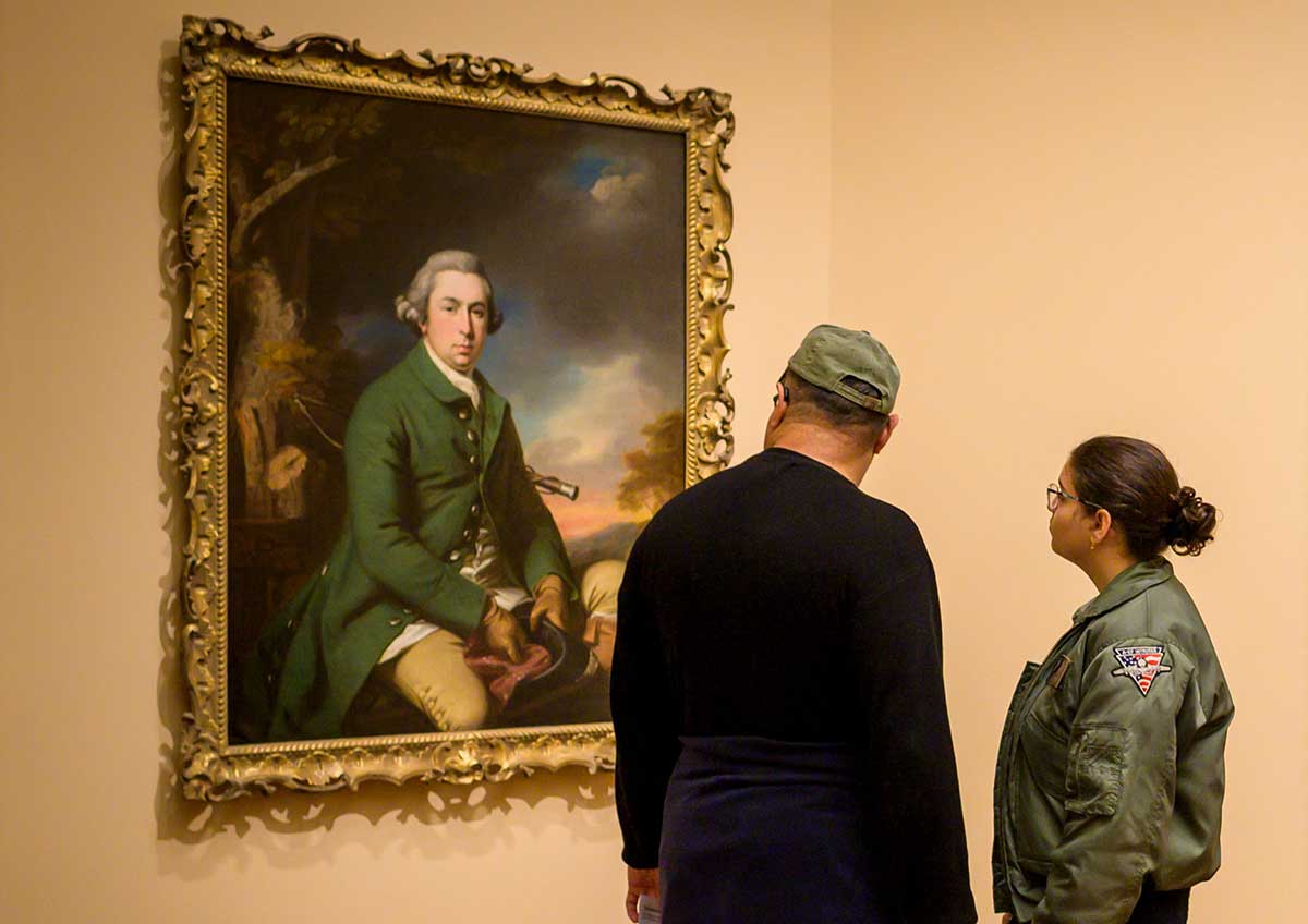 Two visitors stand together viewing a painting in a gallery